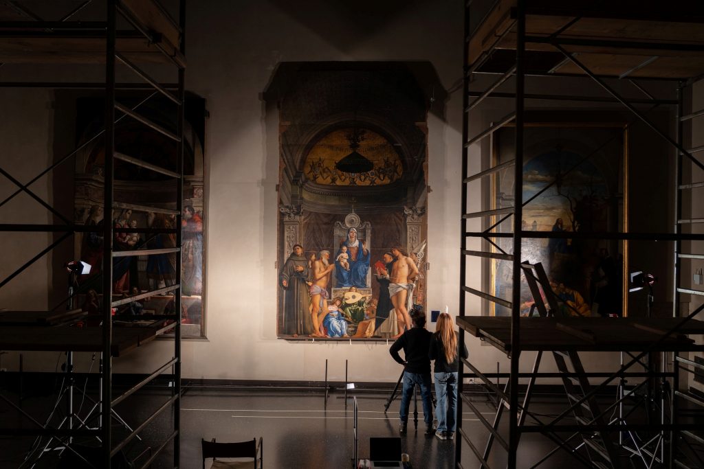 two people standing in front of a large painting with scafolding around them
