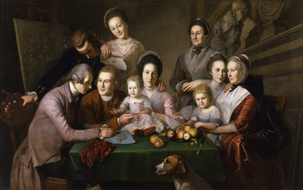a painting of a large white family group gathered around a table in an 18th-century interior, including men, women, and children; one man sketches at the table while others look on, with fruit, a small dog, and sculpted busts in the background, creating a lively, intimate domestic scene