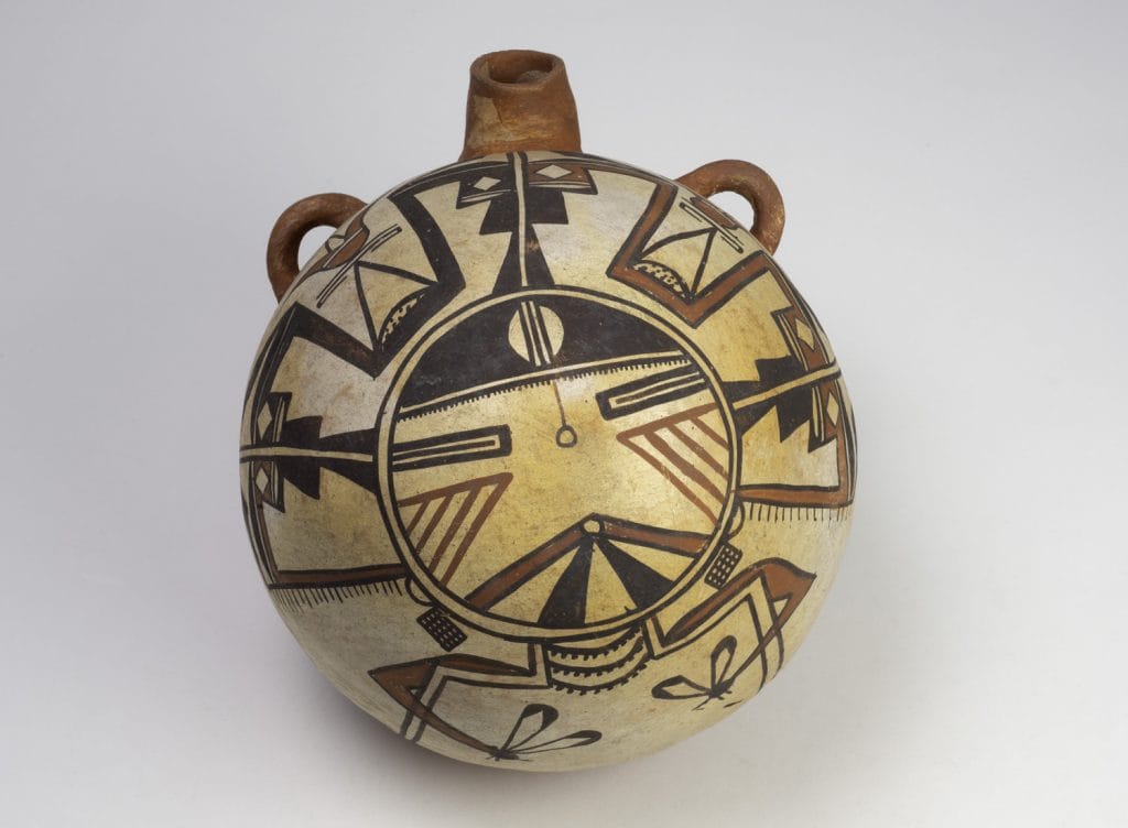 Painted Native American ceramic vessel with a rounded body, short neck, and two small side handles, decorated with geometric black, red, and cream patterns arranged around a central circular motif.