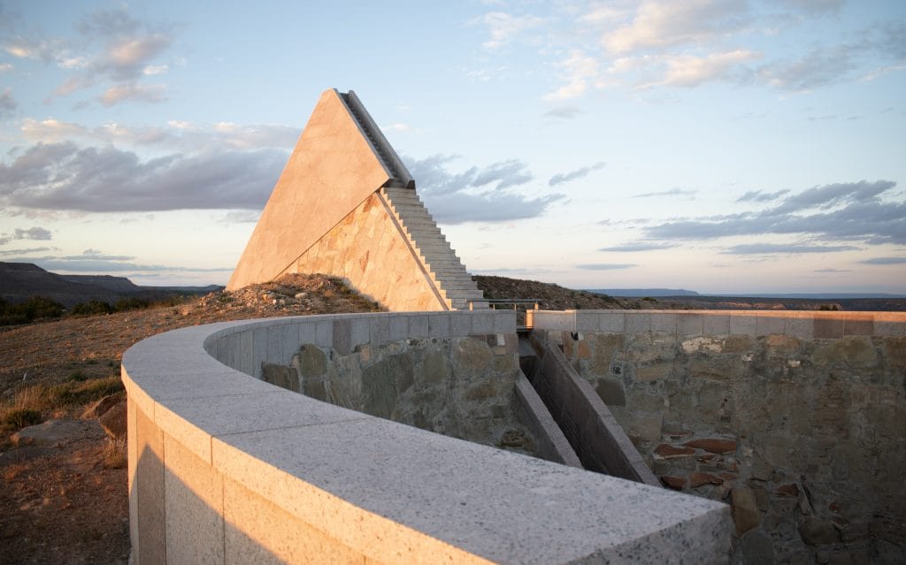A large pyramid-shaped structure in a desert landscape, with a staircase ascending along one side.