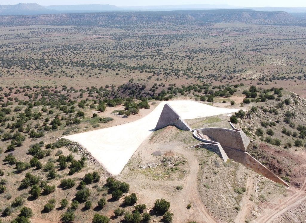 Aerial view of a desert installation featuring a triangular structure and surrounding earthworks set in a vast, arid landscape.