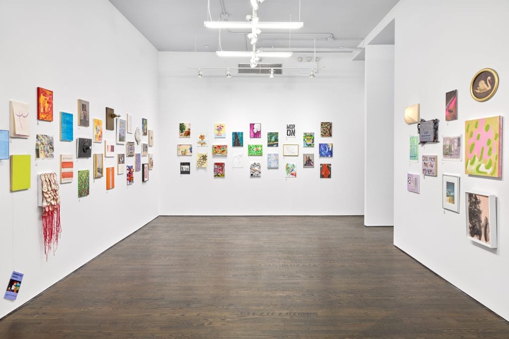 A photo of a white cube gallery space with rows of small, colorful rectangular paintings hung on the wall in a neat grid.