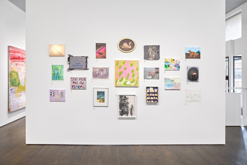 A photo of a white cube gallery space with a nearly hung arrangement of small, colorful rectangular paintings. 