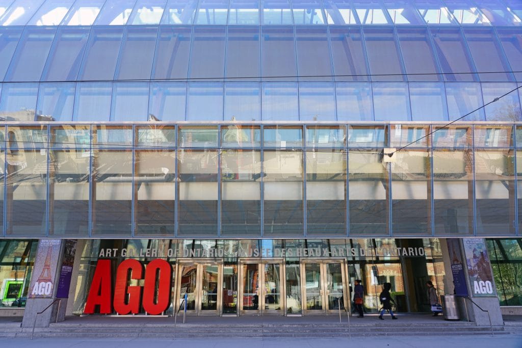 Modern glass facade of Art Gallery of Ontario with large red AGO sign, entrance doors, pedestrians walking