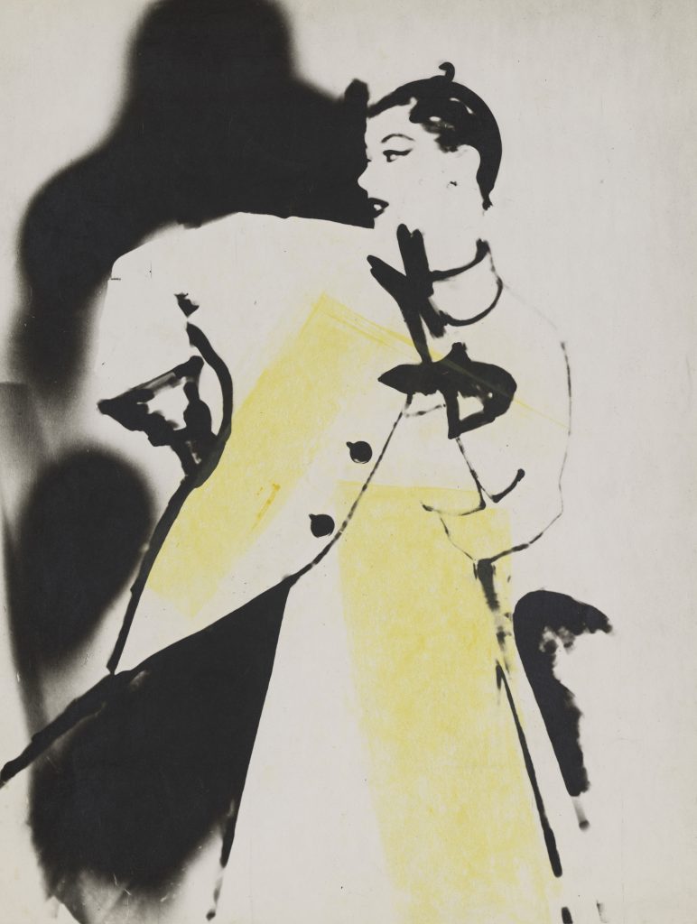 Stylized black-and-white photograph of a woman in profile wearing a smock-like coat, rendered in high contrast with soft, blurred edges and accented by a wash of yellow pigment; her shadow looms large behind her.
