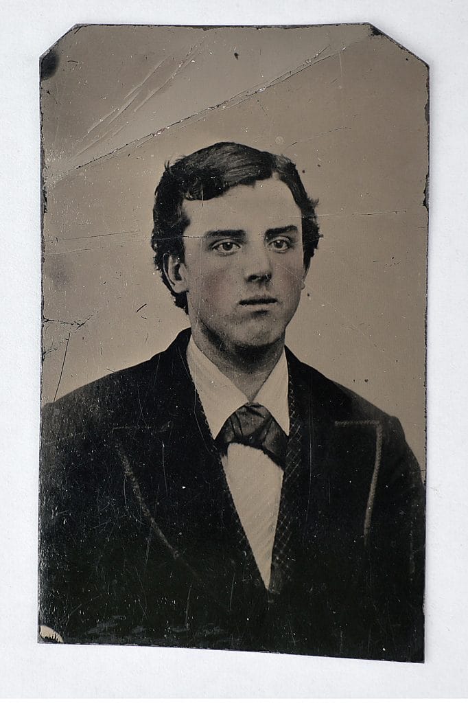 Worn tintype portrait of young man in suit, cracked surface, formal pose, nineteenth-century photograph