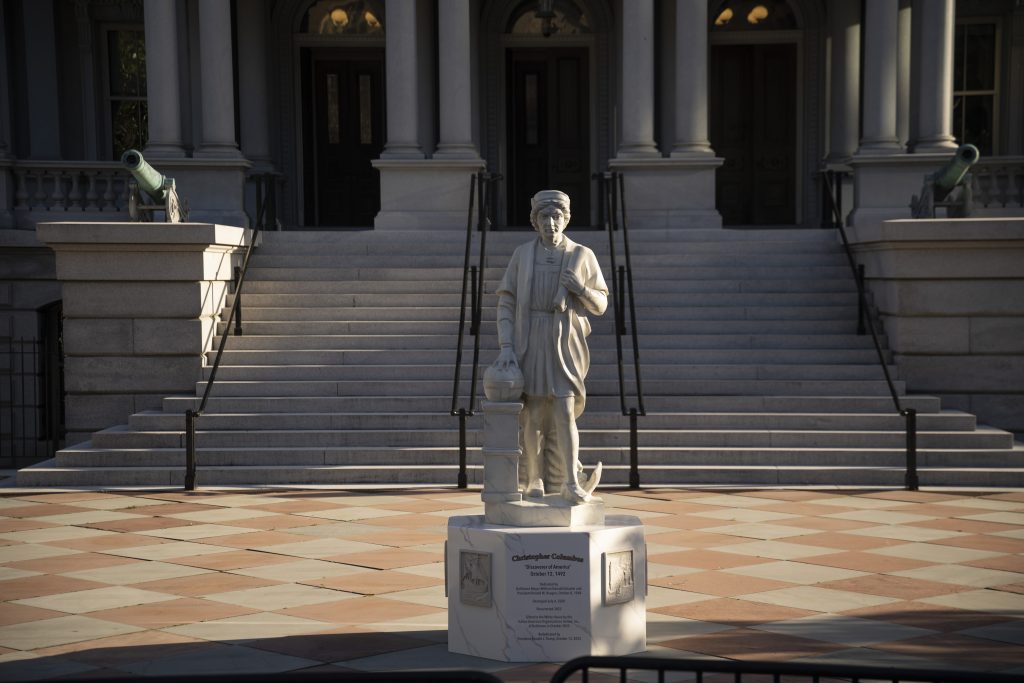 Statue of Christopher Columbus standing before grand staircase and columns, flanked by cannons outside building