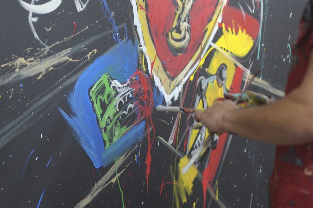 Painter’s hand applies vivid, chaotic strokes on abstract canvas, splashing bright colors across textured surface