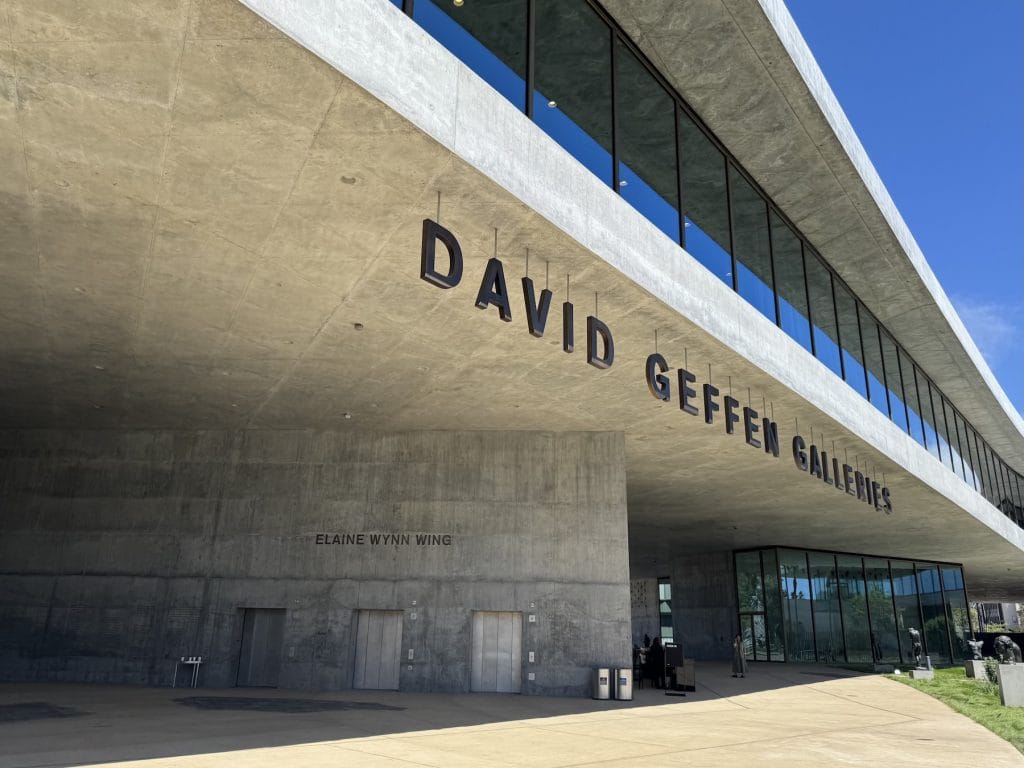 The modern concrete exterior of the David Geffen Galleries features a large overhanging roof with the building's name in bold letters above the museum entrance.