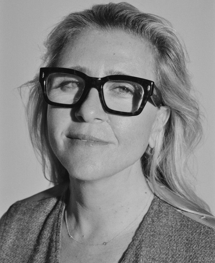A black and white headshot of a woman with blond hair and thick black glasses