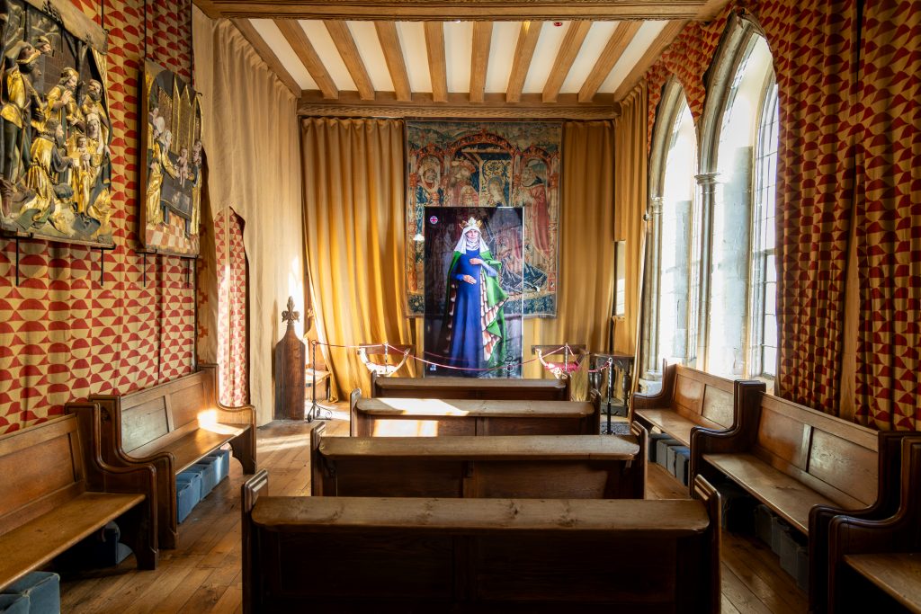 Historic chapel interior with wooden pews and large screen displaying AI medieval queen figure.