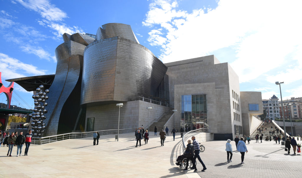 Exterior view of the Guggenheim Museum Bilbao with visitors walking across the plaza on a sunny day.