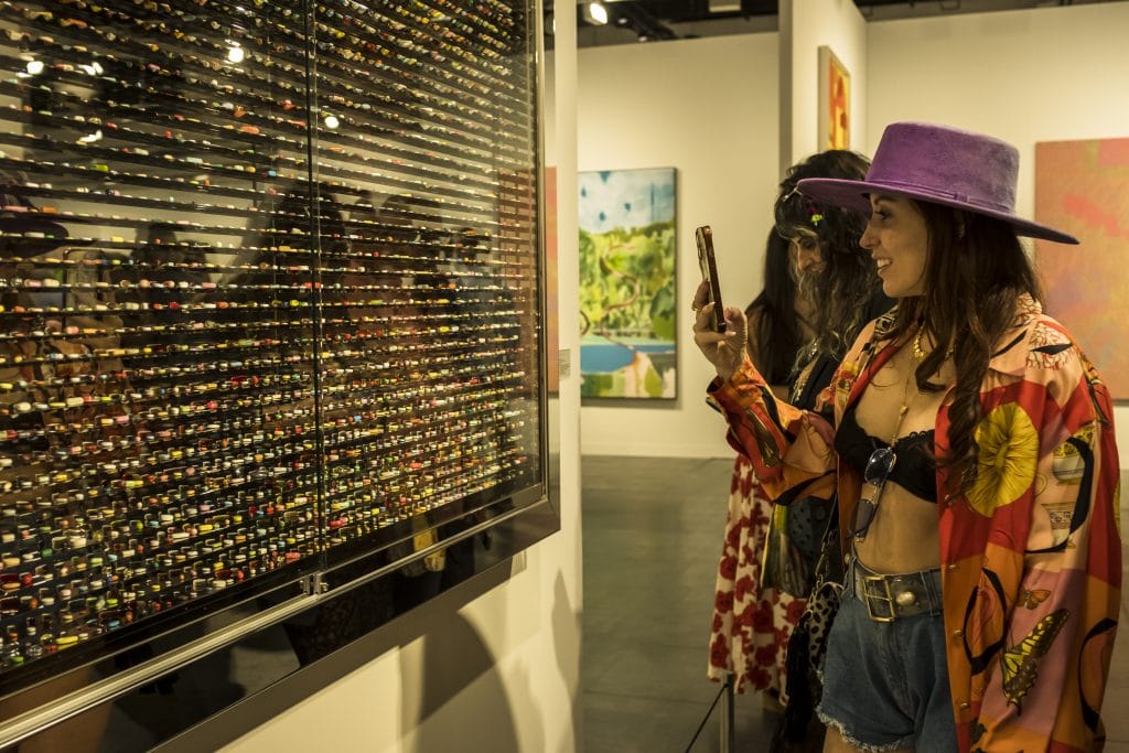 A lady takes a photo of a shimmering, shiny artwork lined with gems.