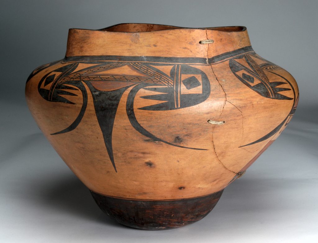 Wide, low Native American pottery jar with a slightly flared rim, featuring black painted bird motifs on a warm brown surface; visible cracks and repairs along the side.