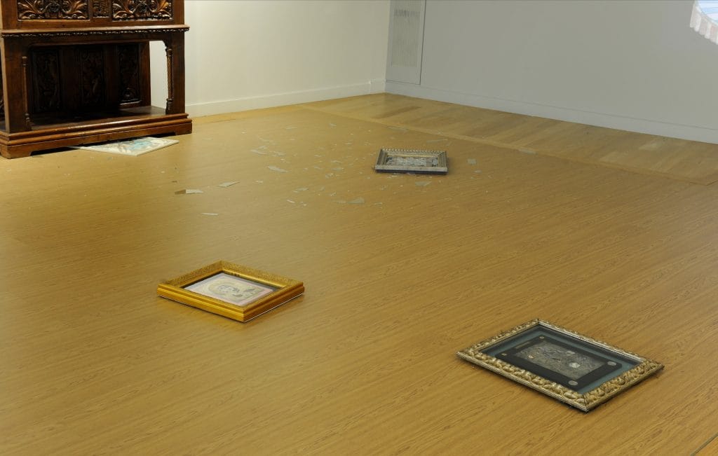 some framed artworks lying on the floor, some are surrounded in shards of smashed glass due to being thrown on the floor