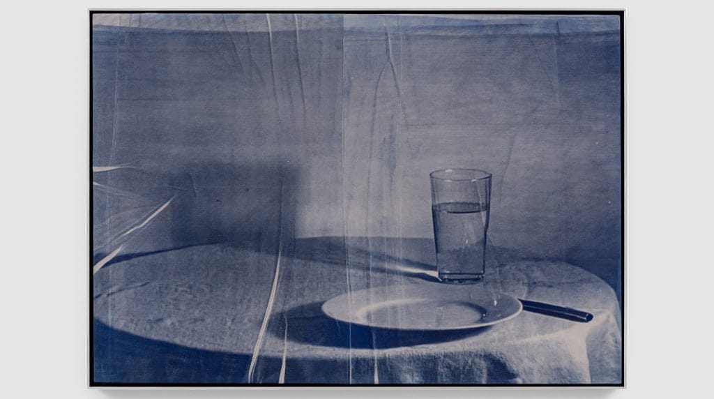 a framed still-life image of a plate and a glass of water on a table with a white tablecloth, the image is grey tinted