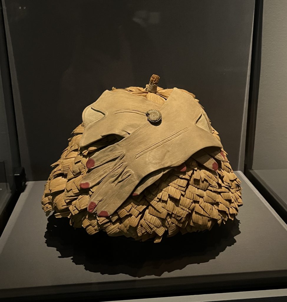 a mound of aged brown fabric is topped by two limp gloves that have the finger tips painted red