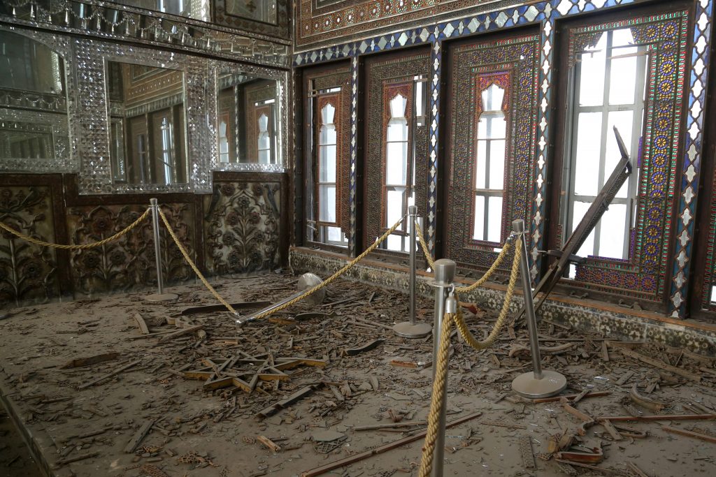 Damaged palace room with shattered inlay floor debris, ornate windows, and protective ropes cordoning area.