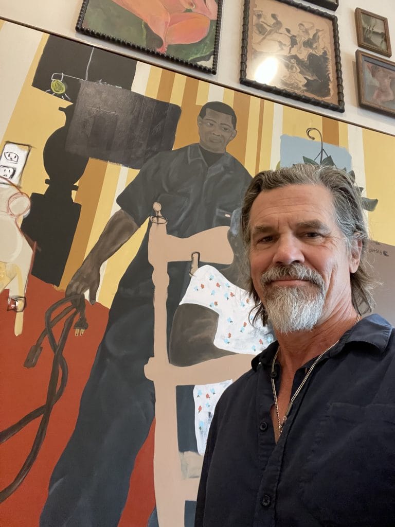 A bearded Josh Brolin standing in front of a vivid Jammie Holmes painting of a Black man standing alongside an elderly woman