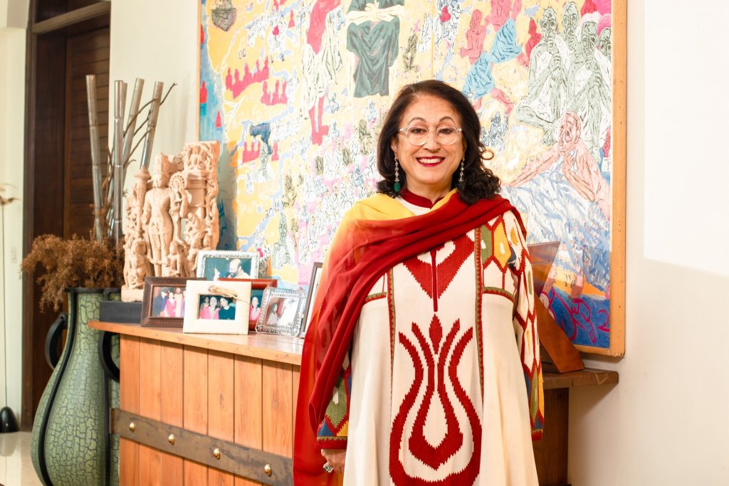 An Indian woman, Kiran Nadar, smiles for the camera, with artworks in the background