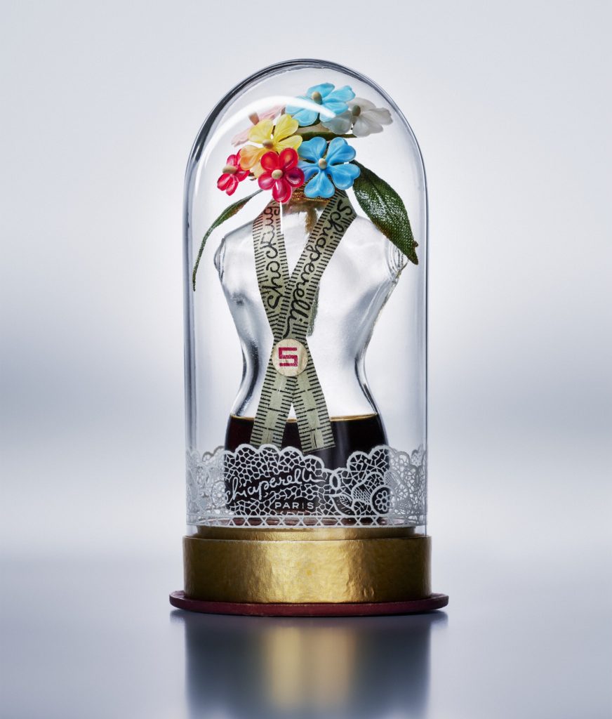 a photograph of a perfume bottle in the shape of a woman's torso, it is inside a glass dome