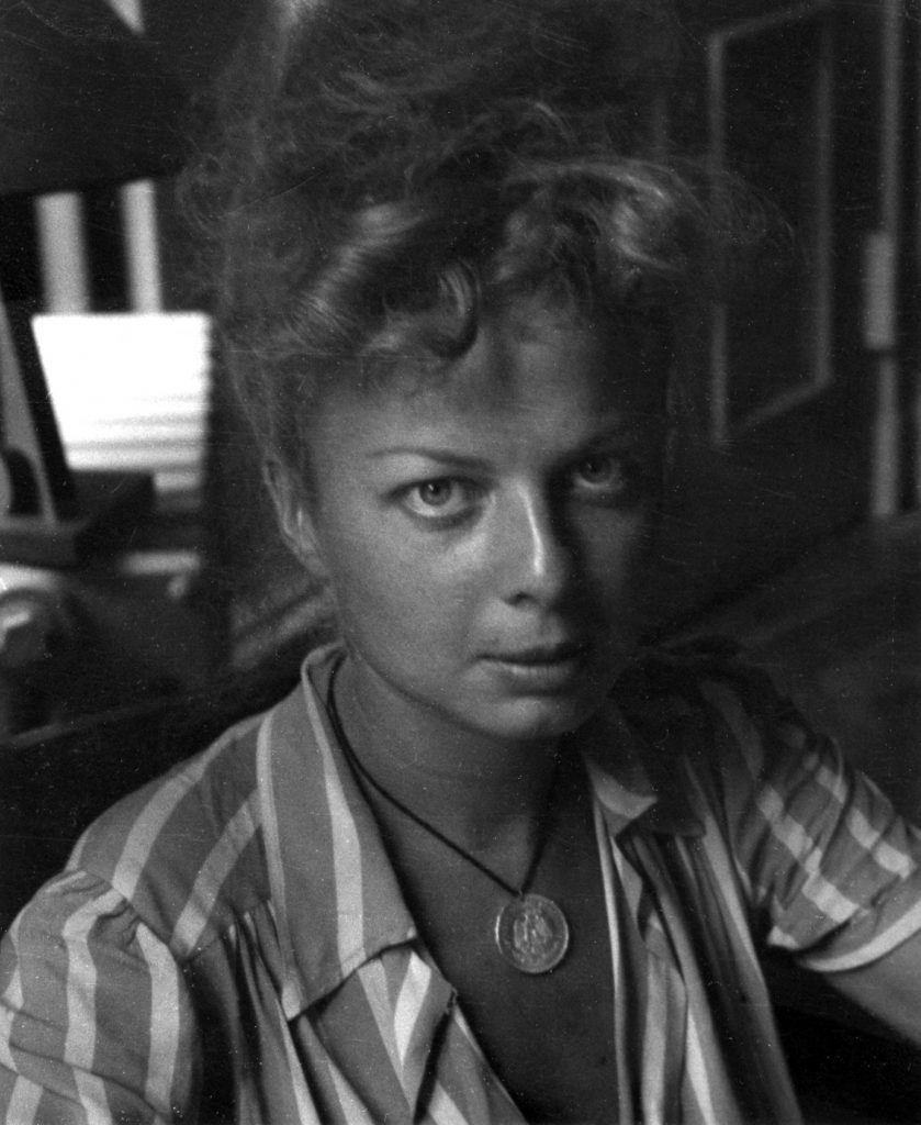 Black-and-white portrait of a young Lillian Bassman in profile, her hair softly curled, gazing downward with a contemplative expression against a plain background.