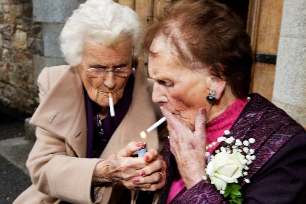two elderly women light cigarettes, they are well dressed and made up