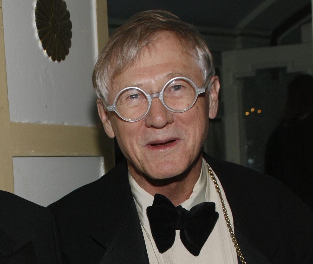 A photo of an older white man with light hair and round eyeglasses, smiling slightly while dressed in a black tuxedo with a bow tie. He appears to be at an indoor event or gathering.