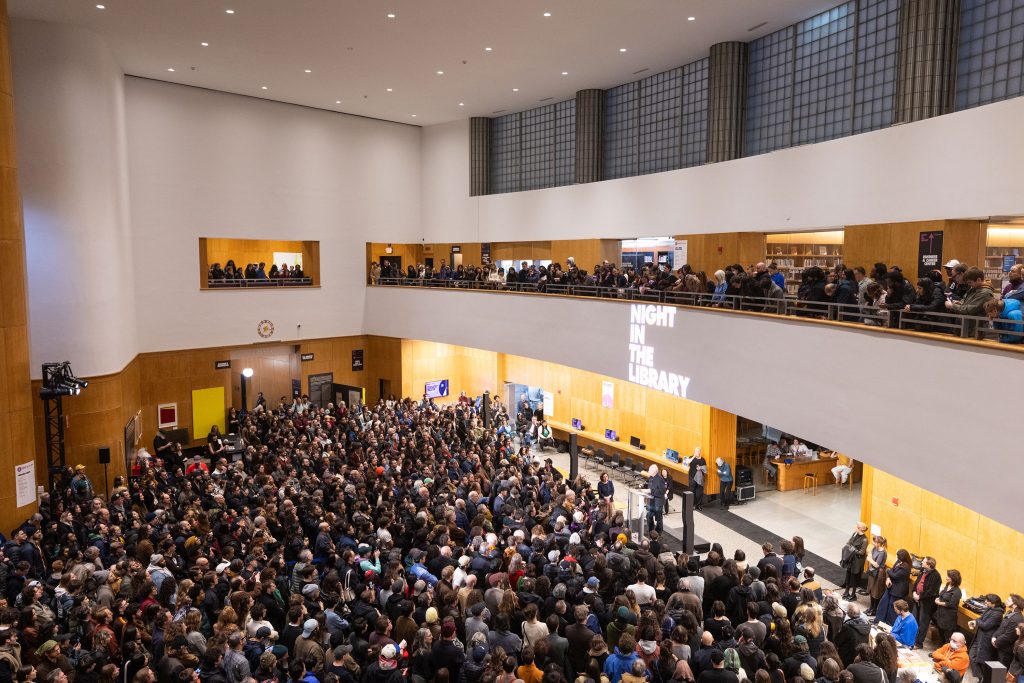 Large crowd gathers across multiple levels inside library atrium during Night in the Library event.