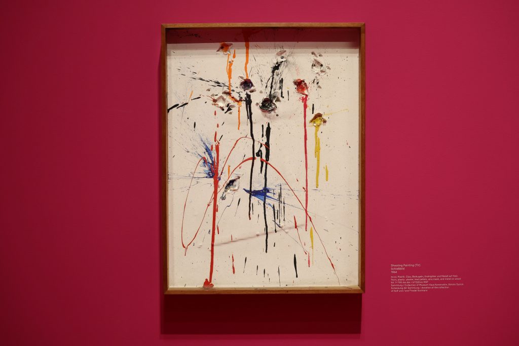Framed Niki de Saint Phalle shooting painting displays punctured surface with dripping paint against red wall