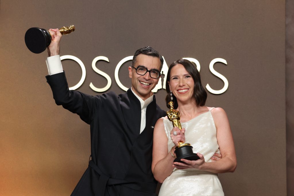 Alexandre Singh and Natalie Musteata pose in front of an Oscars backdrop, each holding an Oscars statuette