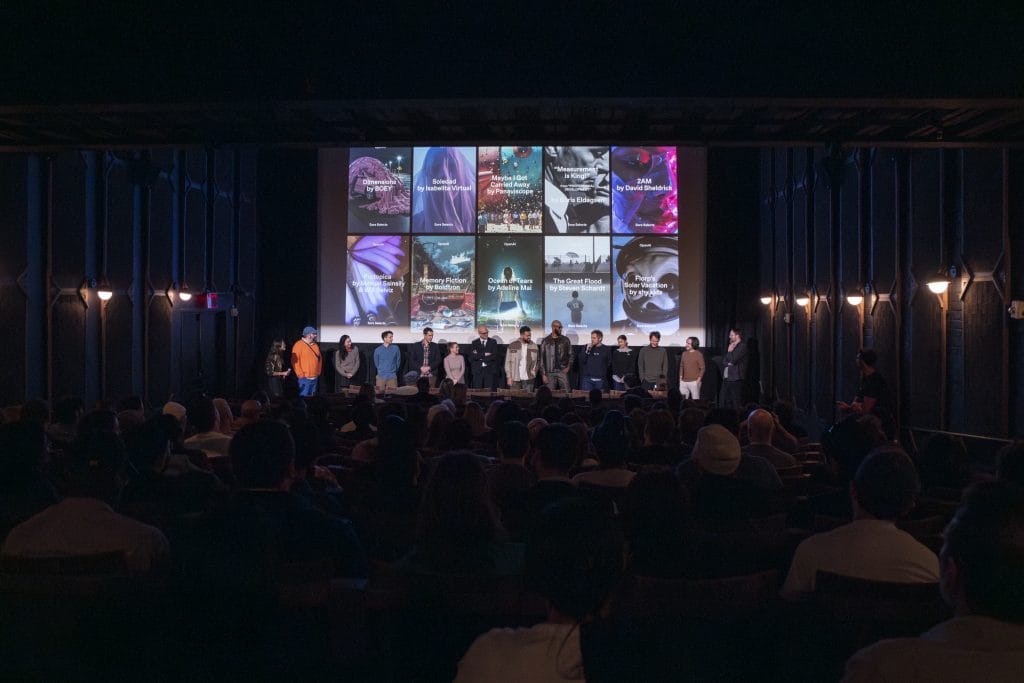 A row of people standing in front of a big screen in a theater sora