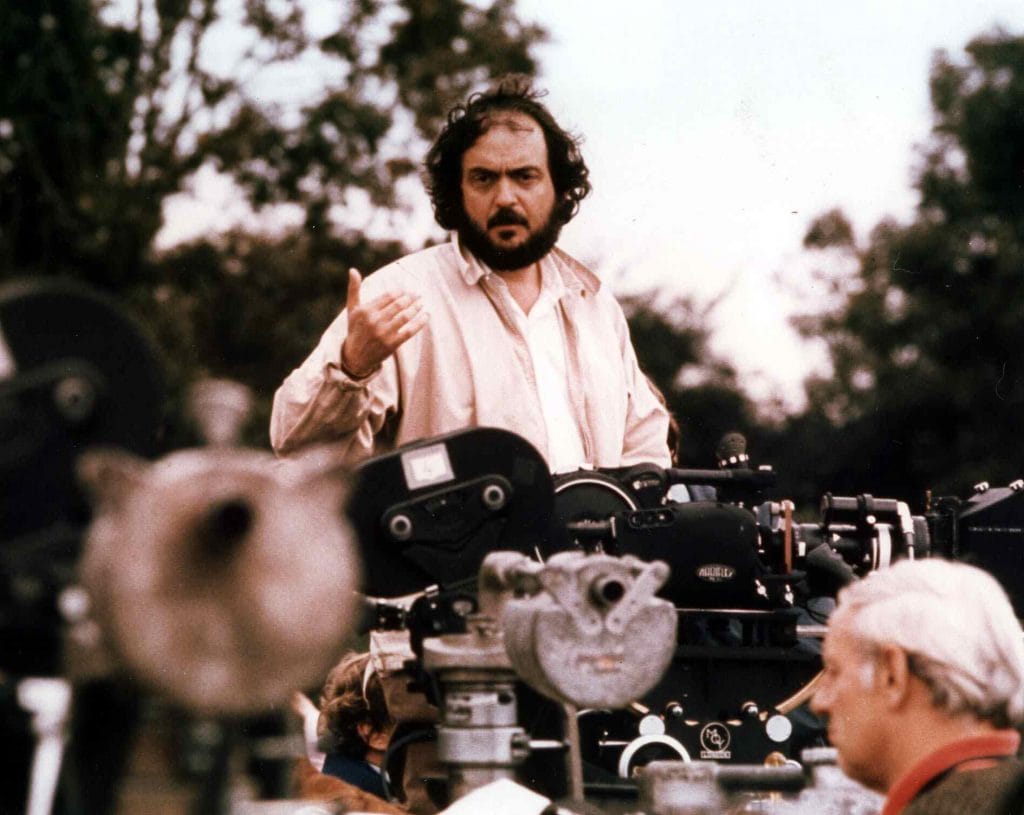 Stanley Kubrick on the set of a movie, standing amid a bank of cameras and gesturing