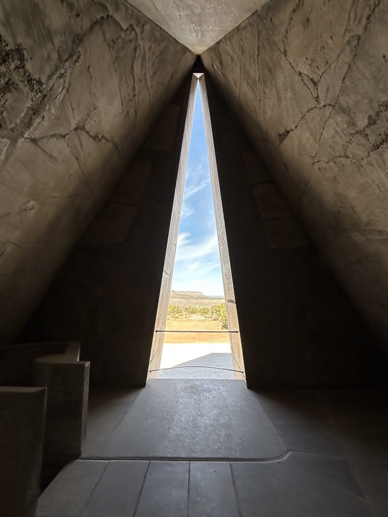 nterior stone stairway leading upward toward a circular opening framing the sky, illuminated by soft natural light.