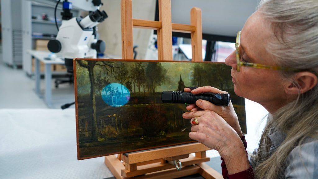 a woman holds a pen with a special light and shines it on a painting